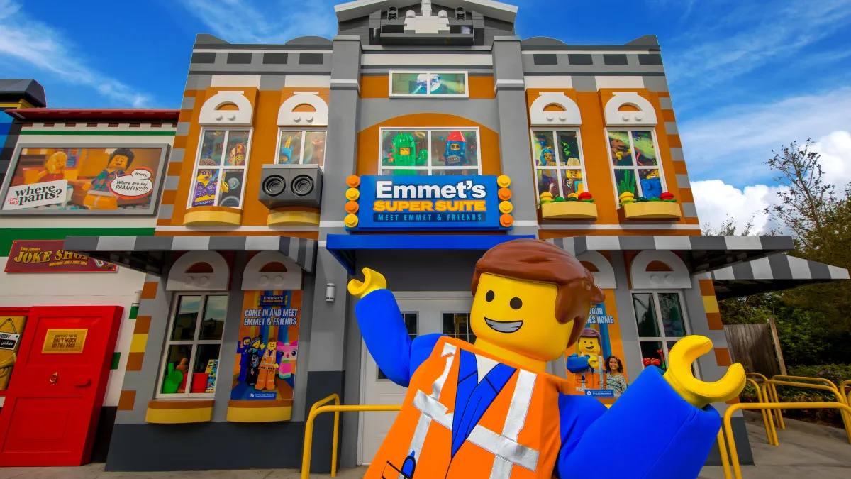 Emmet stands in front of Emmet's Super Suite at LEGOLAND California's LEGO Movie World, showcasing a vibrant LEGO landscape.