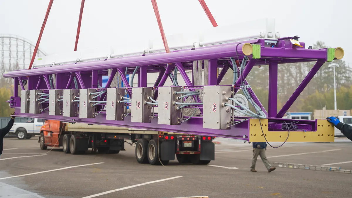 workmen unload a piece of purple coaster track from a truck arriving from Europe.
