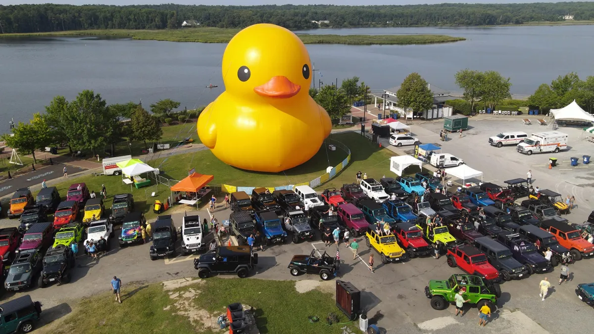 A giant inflatable duck sits along the edge of a lake.