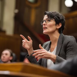 Female politician in legislative chamber speaking passionately