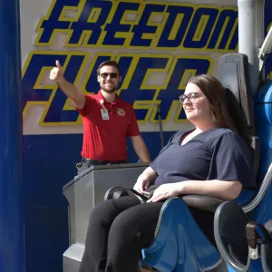 Amusement Ride Operator showing Thumbs Up while a Woman is sitting in a roller coaster train with the restraints closed