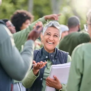 Woman with short white hair holding pen and paper, smiling with co-workers