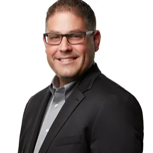 Adam Gross, smiling, wearing glasses, button down, and suit jacket