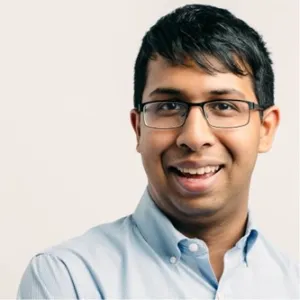 1. A man wearing glasses and a blue shirt smiles warmly at the camera.