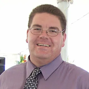 Greg Morrow smiling, wearing purple dress shirt and checkered tie