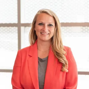 A woman dressed in an orange blazer and gray shirt, showcasing a professional appearance and poised demeanor.