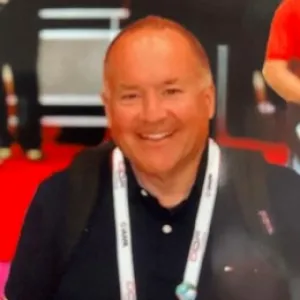 A smiling man dressed in a black shirt and red tie poses for the photo