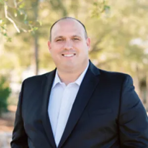  A man in a suit and tie stands confidently in front of lush green trees