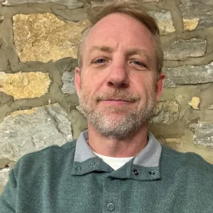 A bearded man dressed in a green shirt, looking relaxed and friendly