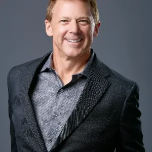A man in a suit smiles warmly at the camera, exuding confidence and professionalism.