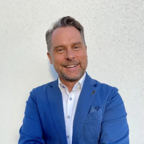 A professional headshot of Pat Idzikowski wearing a white shirt and blue suit