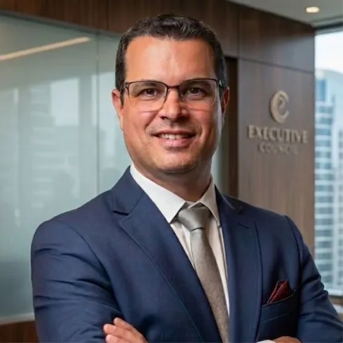Ivan standing in front of an office, smiling at the camera, arms crossed, wearing a dark blue suit with a grey tie