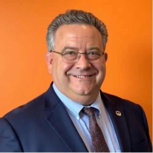 Jason smiling at the camera in front of an organ wall, wearing a dark blue suit and tie
