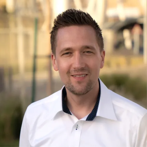 Neil wearing a white shirt smiling at the camera in front of a blurry background