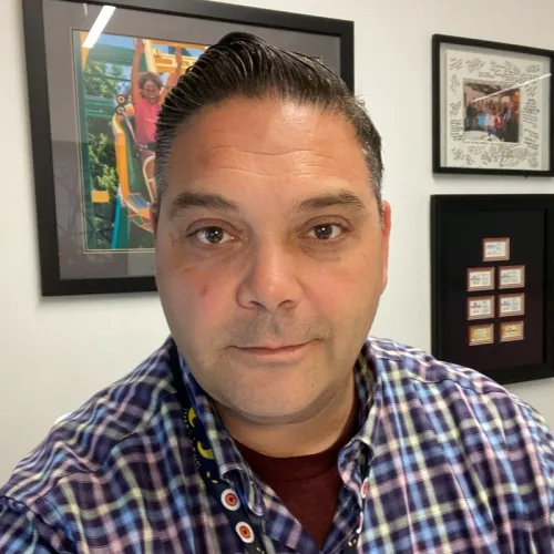 Randall smiling at the camera in front of a wall with pictures, wearing a chequered shirt