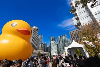 A giant duck sits amongst skyscrapers in a downtown environment.