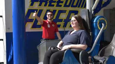 Amusement Ride Operator showing Thumbs Up while a Woman is sitting in a roller coaster train with the restraints closed