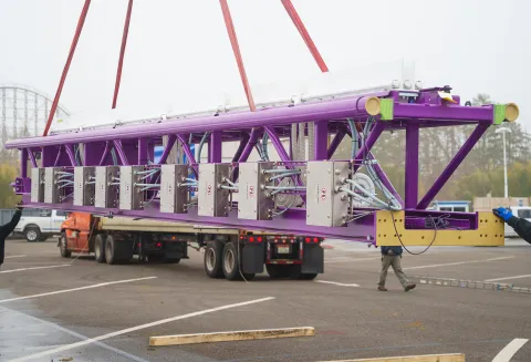 workmen unload a piece of purple coaster track from a truck arriving from Europe. 