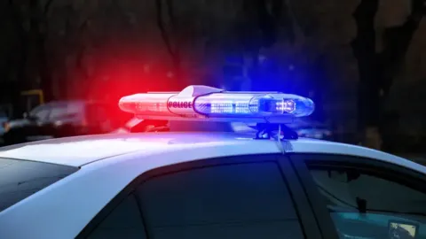 Police Car with swirling red and blue lights on while on an active crime scene