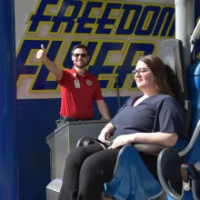 Amusement Ride Operator showing Thumbs Up while a Woman is sitting in a roller coaster train with the restraints closed