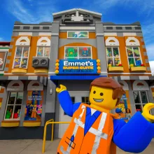 Emmet stands in front of Emmet's Super Suite at LEGOLAND California's LEGO Movie World, showcasing a vibrant LEGO landscape.